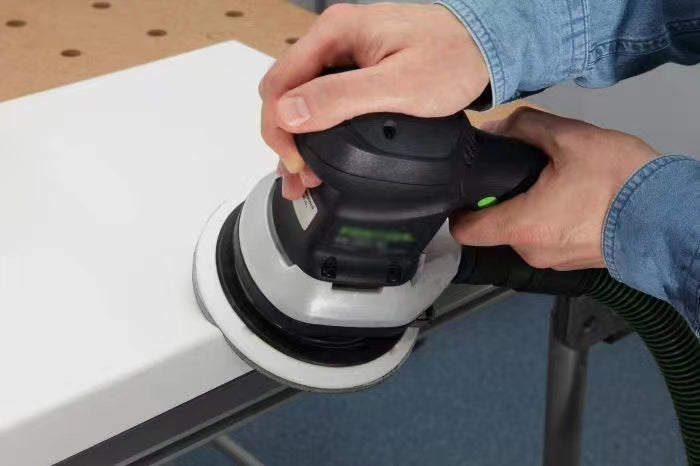 Worker using a powered sander to finish a white solid surface panel