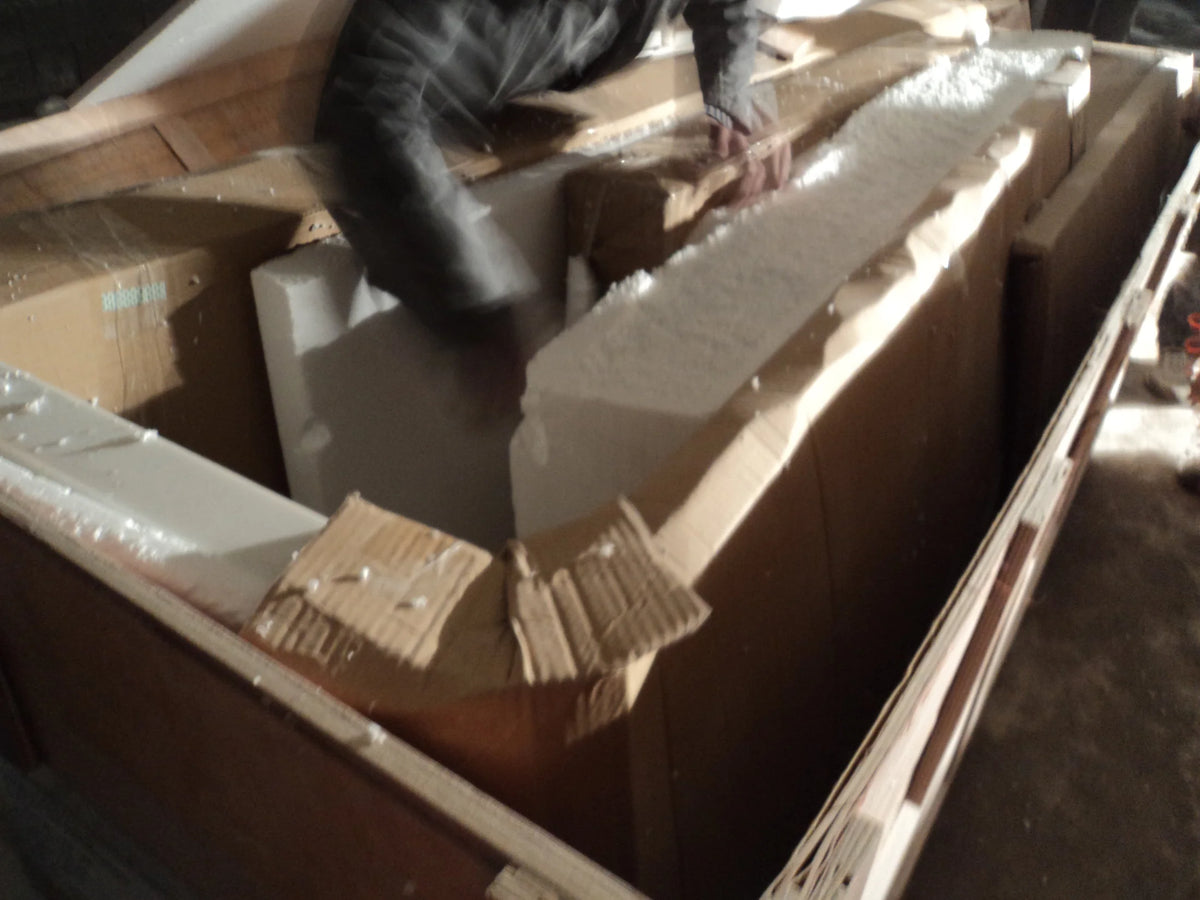 Protective cardboard and foam fitted around furniture components inside an open wooden crate